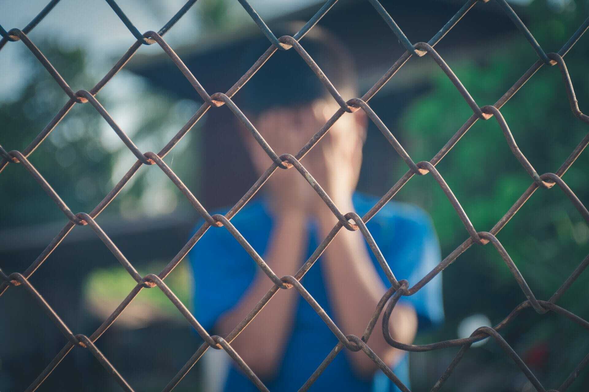 asian kid boy crying behind a metal chain wire mesh fence
