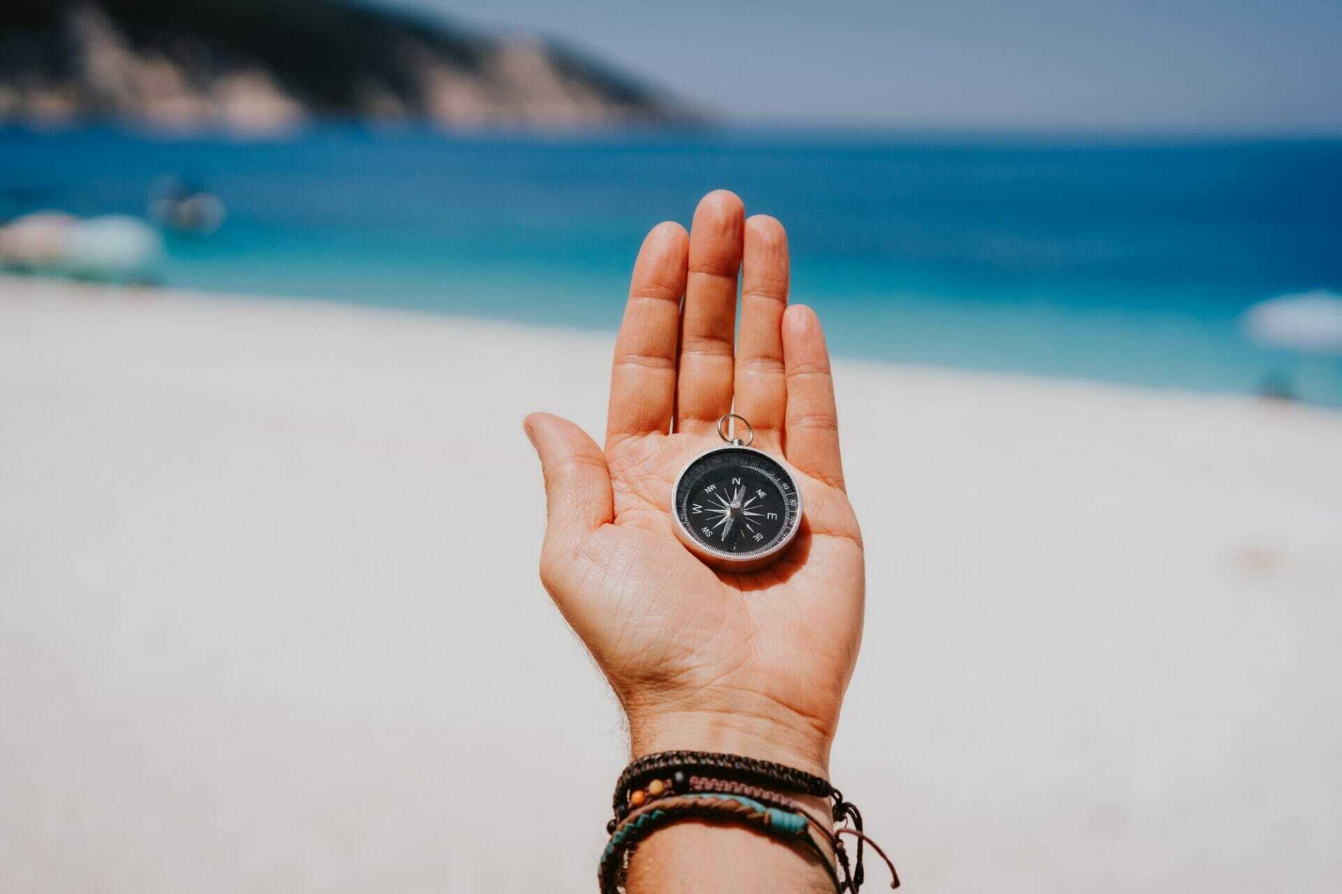 stretched hand palm with black metal compass against summer beach and blue sea follow your way